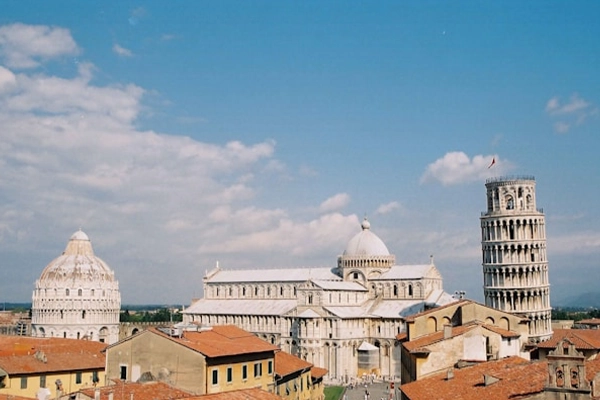 The distant view of the Leaning Tower of Pisa over rooftops. Clear sky and landscape.