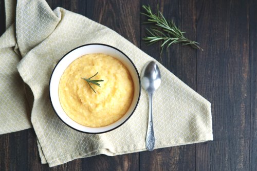 Creamy corn traditional polenta or mamaliga with butter. Served in white shallow dish on rustic wooden table with rosemary. Country style. Selective focus, copy space, top view. Healthy food conce
